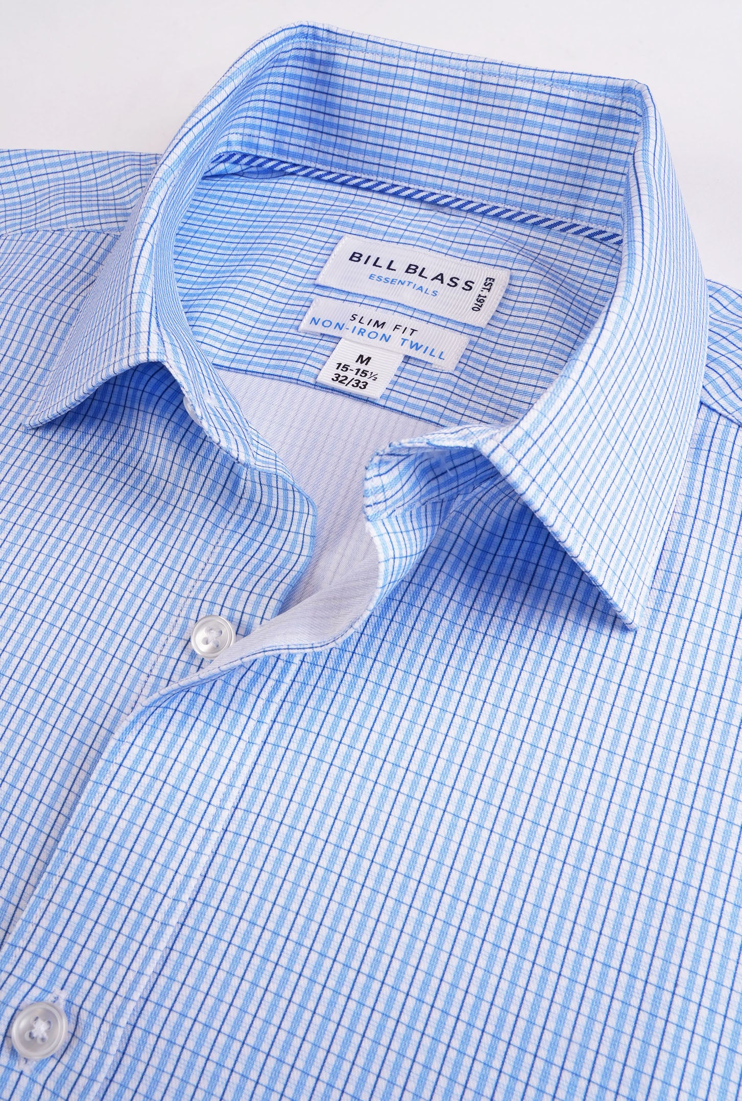 Close-up of a blue checkered shirt with 'Bill Blass' label on a light gray background